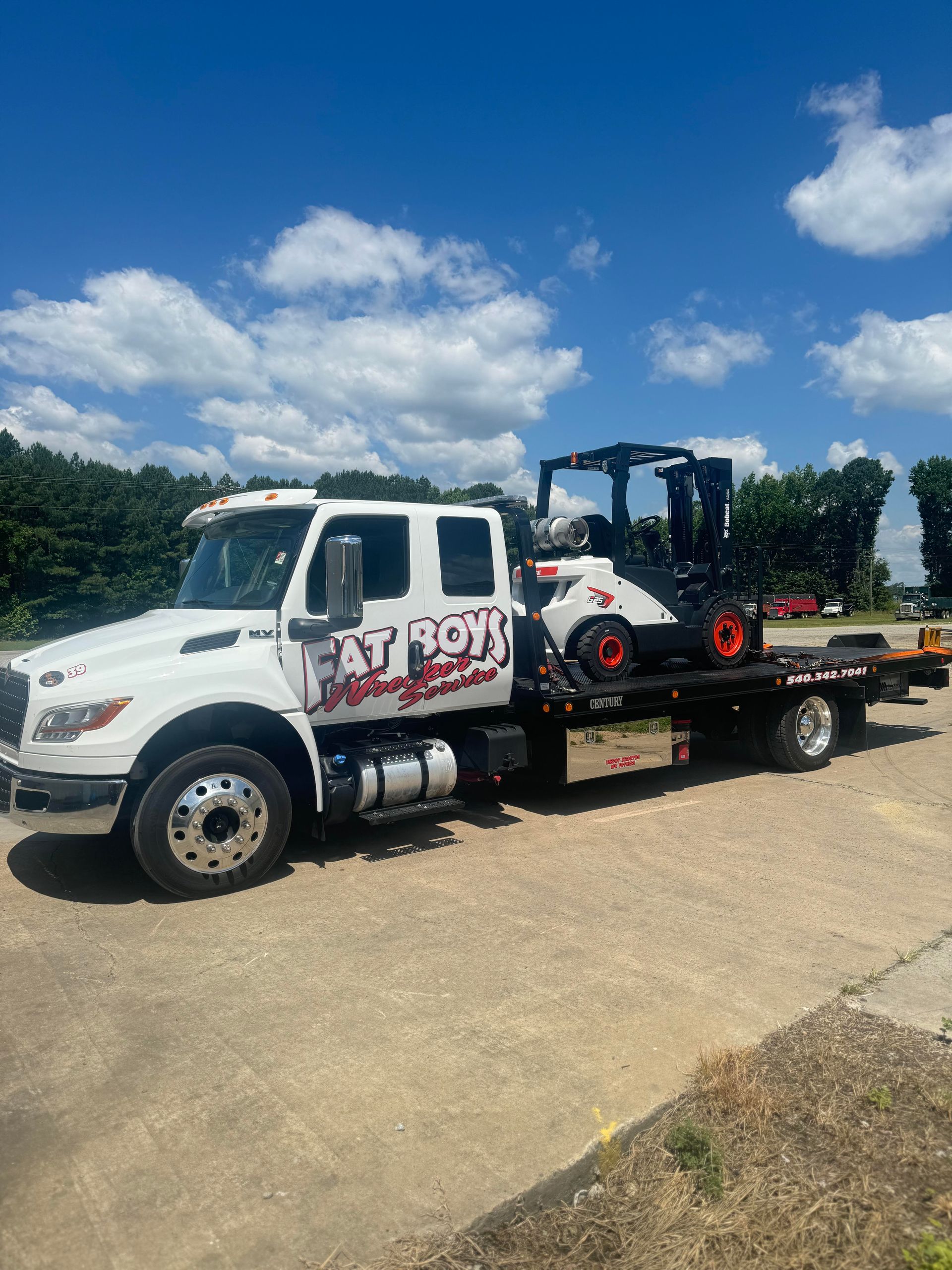 A white tow truck is carrying a forklift on the back of it.