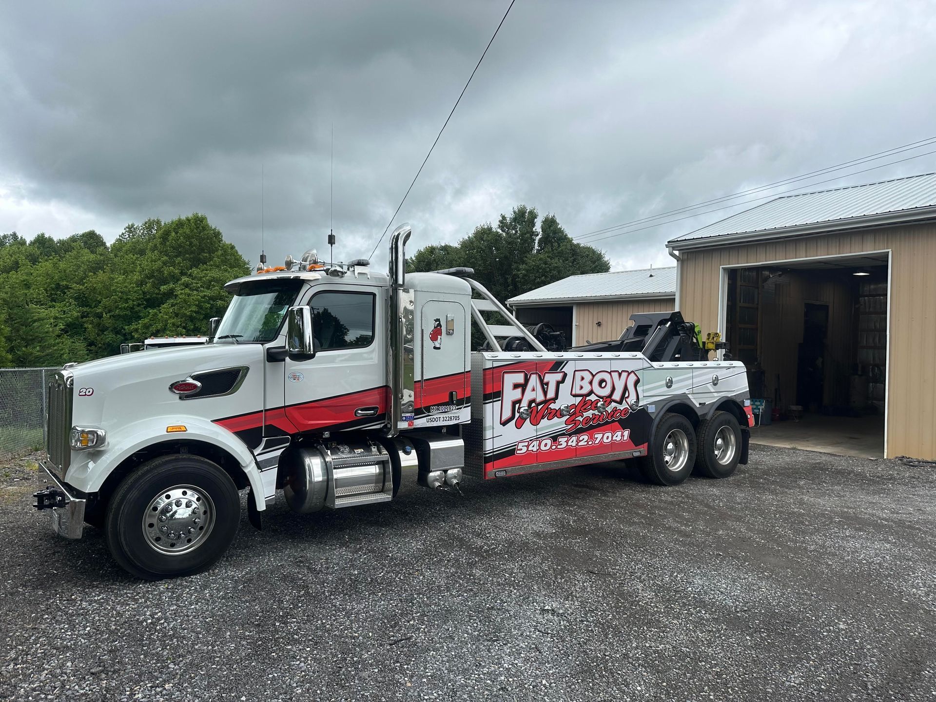 A white and red tow truck is parked in front of a garage.