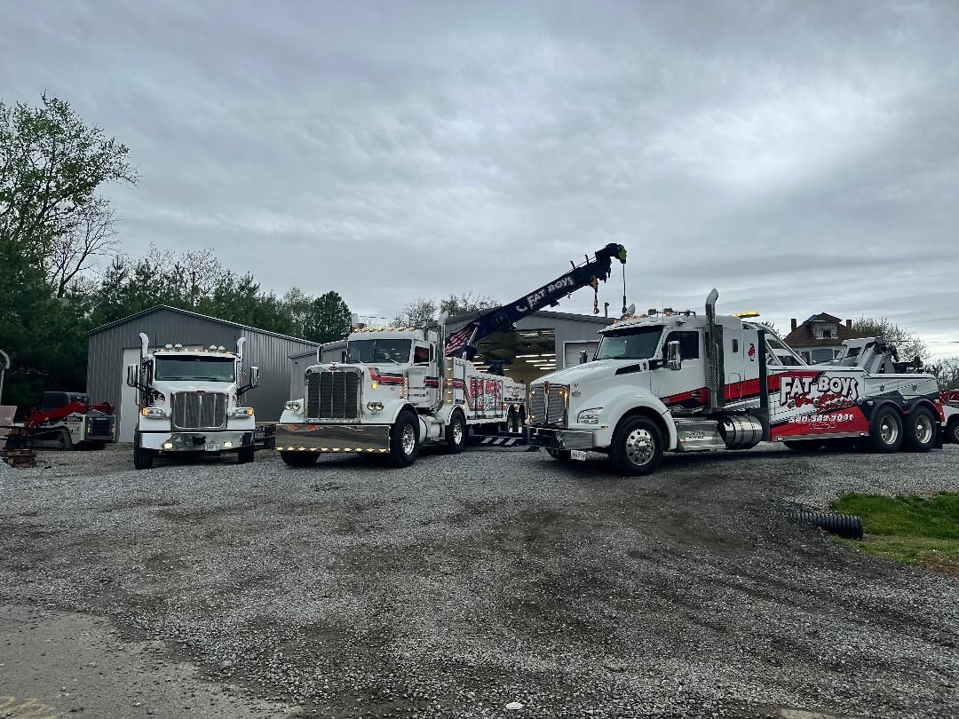 A row of tow trucks are parked in a gravel lot.