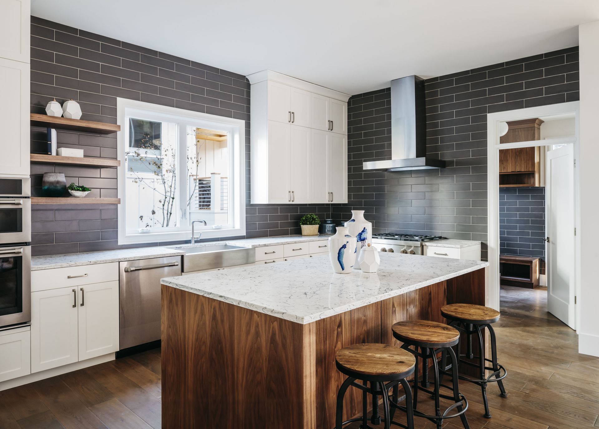 A modern kitchen featuring a dark tile backsplash, white cabinetry, a walnut kitchen island, and three wooden stools.