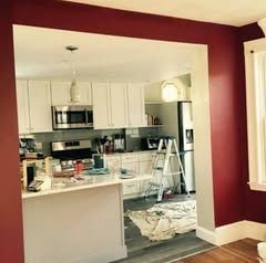 A kitchen seen through a doorway with white cabinets and a center island, set against deep red walls in the foreground.
