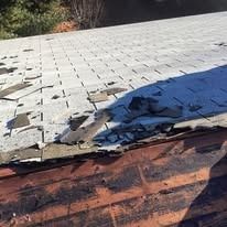 Damaged roof with missing and broken asphalt shingles exposing the wood decking underneath.