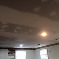 A ceiling with patches of wet or discolored drywall in a room with recessed lighting and a window.