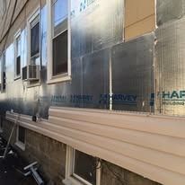 A side view of a building under construction, featuring silver insulation panels covered by partially installed beige siding.