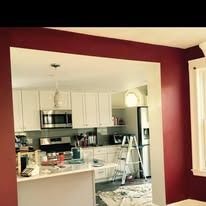 A view from a maroon-walled room into a kitchen with white cabinets, stainless steel appliances, and a step ladder.