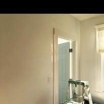 A room with beige walls and a doorway leading to a blue door, with a silver step ladder standing in the foreground.