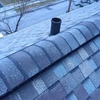 A close-up view of a shingled roof ridge with a dark circular plumbing vent pipe protruding from the roof slope.