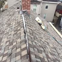 A roof showing a damaged valley with missing shingles, exposed underlayment, and a chimney in the background.