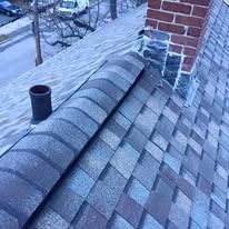 A high-angle view of a grey shingled roof featuring a brick chimney with damaged flashing and a black pipe vent.