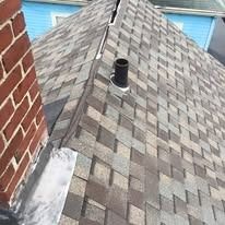 A close-up of a residential roof with asphalt shingles, a brick chimney, a vent pipe, and metal flashing.