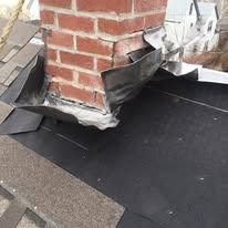 A brick chimney on a roof with unfinished metal flashing and sealant applied around the base.