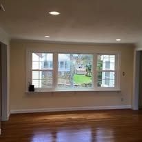 A large, triple-pane window with white frames in a room with light beige walls and polished hardwood floors.