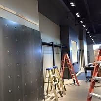 Construction scene with two ladders standing in an empty retail space under renovation, featuring a dark metal wall.