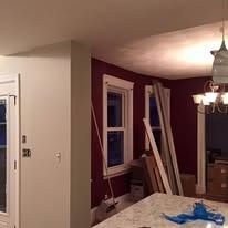 An interior view showing a white wall and a dark red wall with windows, trim pieces leaning against the corner, and light.