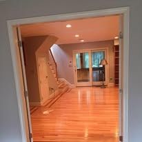 A view through a doorway into a bright room with light wood floors, a staircase, and glass doors leading to the outdoors.