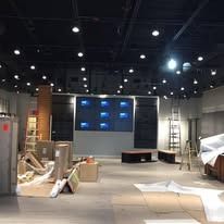 An interior view of a commercial space under construction with exposed black ceilings, a video wall, and equipment boxes.