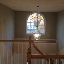 A grand arched window with a lit chandelier hangs above a wooden staircase railing in a residential entryway.