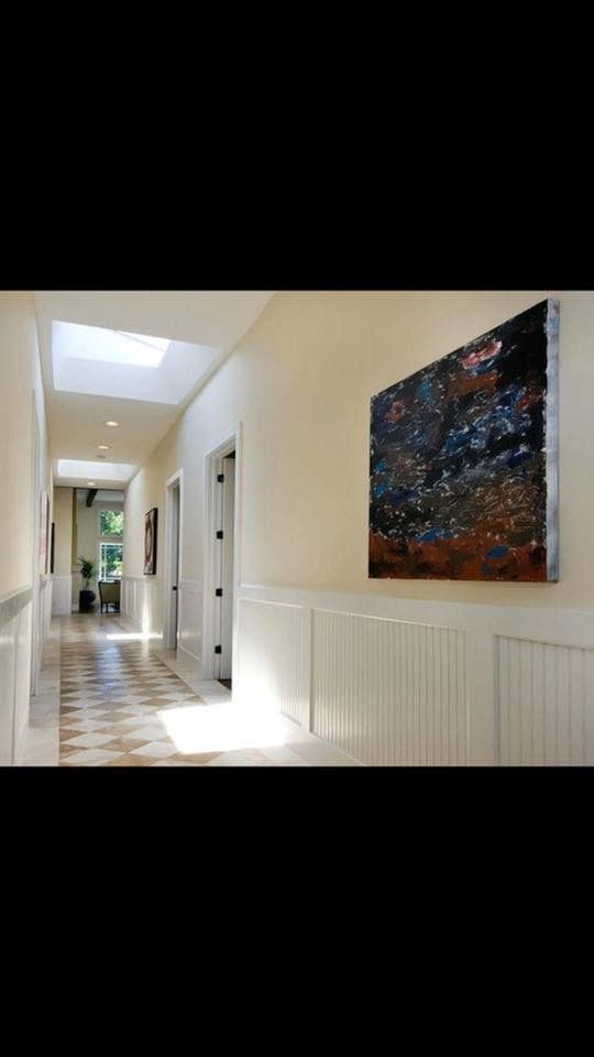 A long, bright hallway with patterned tiled flooring, wainscoting, and a large abstract painting on the wall.