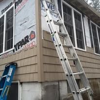 An aluminum extension ladder leans against the corner of a house under renovation with Tyvek house wrap and new siding.