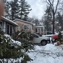 A snow-covered residential area featuring houses and parked vehicles during a winter day.