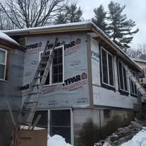 A house exterior under construction with Typar house wrap, windows, and a metal ladder leaning against the side in snow.