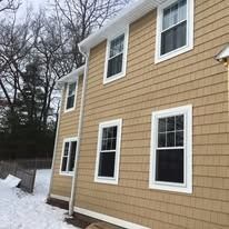 Tan shingle siding on a two-story house exterior with multiple white-framed windows, set against a snowy landscape.
