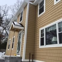 Tan horizontal siding on a two-story house exterior with white trim around windows and a partially framed front entryway.