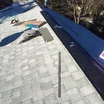 An unfinished roof with light grey shingles, a section of black underlayment, and loose construction materials.