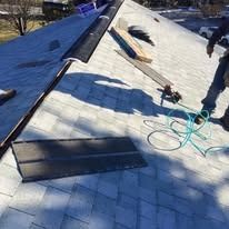 A person installing shingles on a residential roof, with tools and materials nearby.