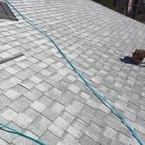 A steep, gray shingled roof with a long green hose stretched diagonally across the surface.