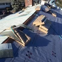 A view of a roof under construction with wooden roof jacks and dark grey protective underlayment on the deck.