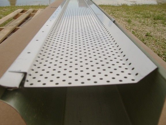 White gutter guard with perforated holes, resting on top of a green gutter, outdoors.