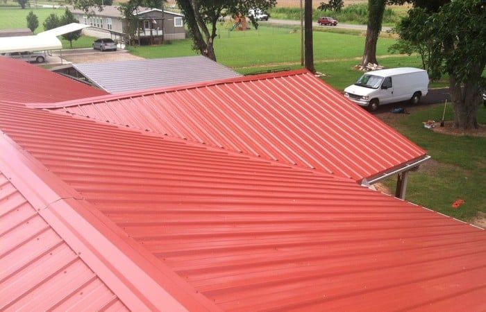 Red metal roof on a building, with a white van parked in the yard.