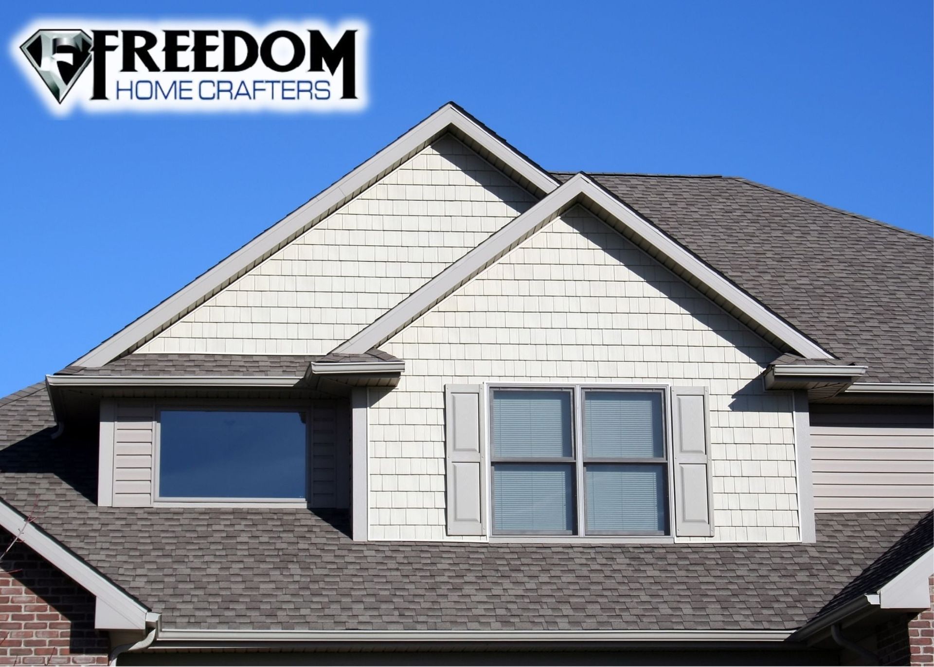 Home with dormers and shingle siding, blue sky background; Freedom Home Crafters logo in the upper left.