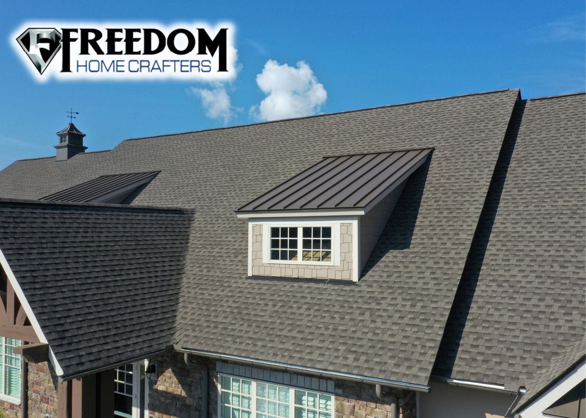 A house with a newly installed dark gray shingle roof, including a dormer with a metal roof and the Freedom Home Crafters logo.