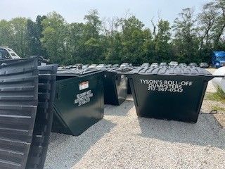 A bunch of dumpsters are sitting on top of a gravel lot.