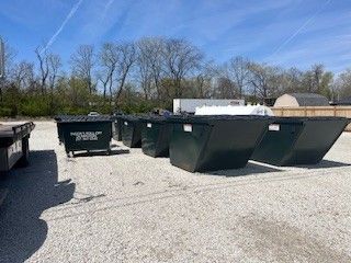 A row of dumpsters are lined up in a gravel lot