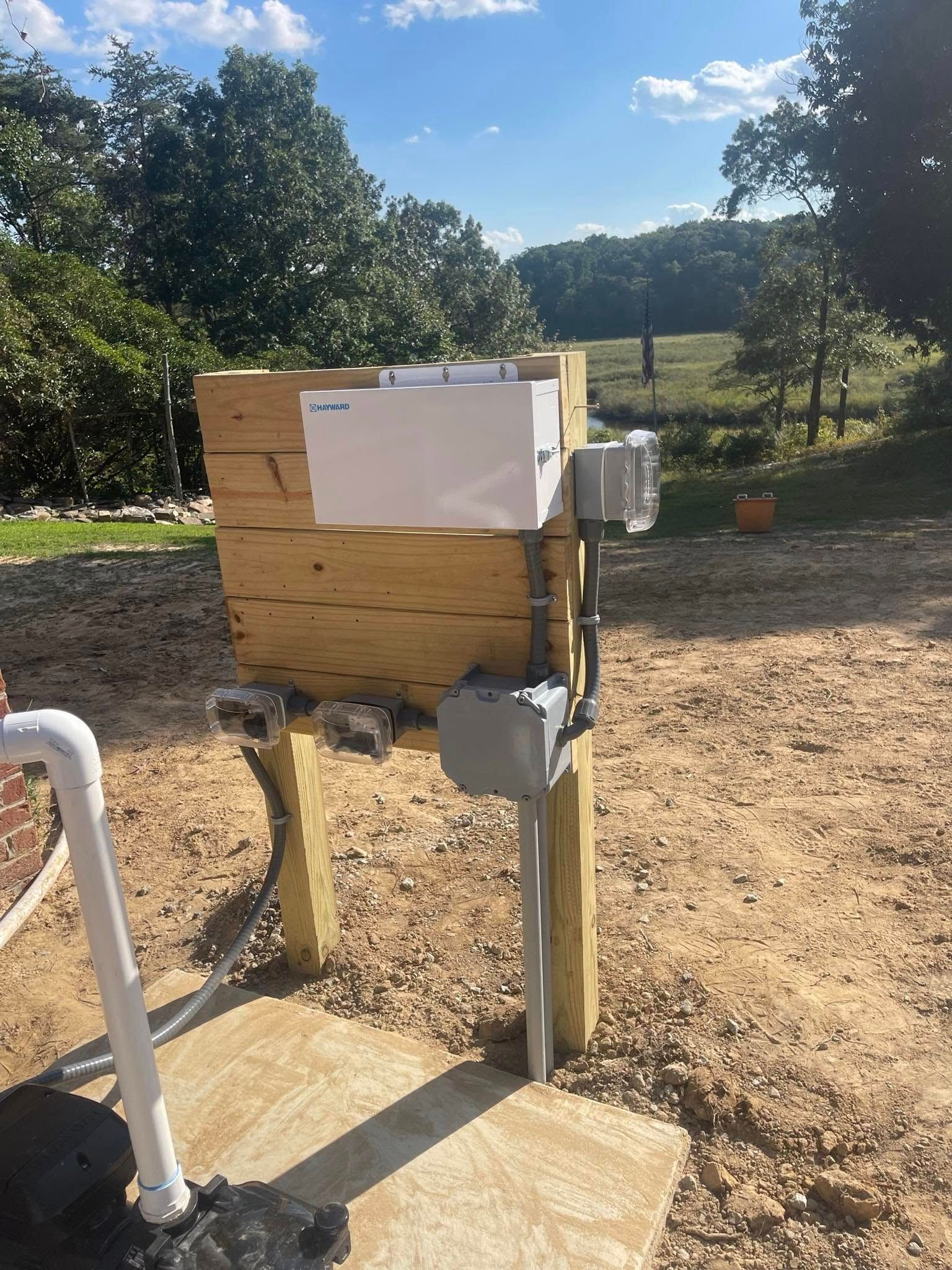 Wooden electrical box with white cover, mounted on posts, in an outdoor setting.