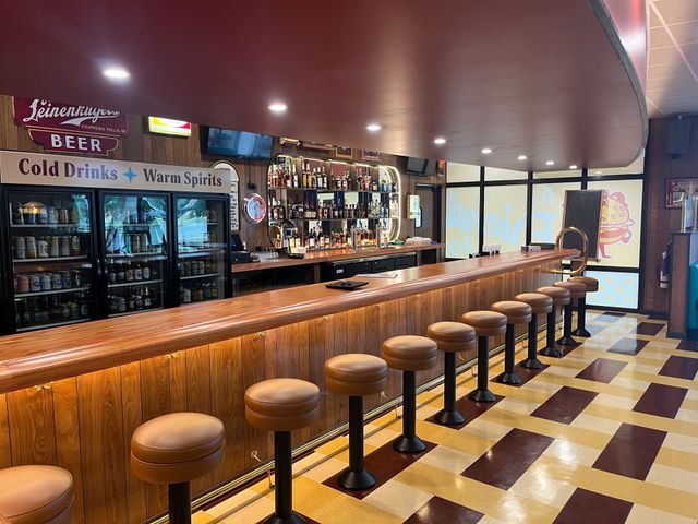 Interior view of a vintage bar with a long counter, stools, and a selection of beverages.