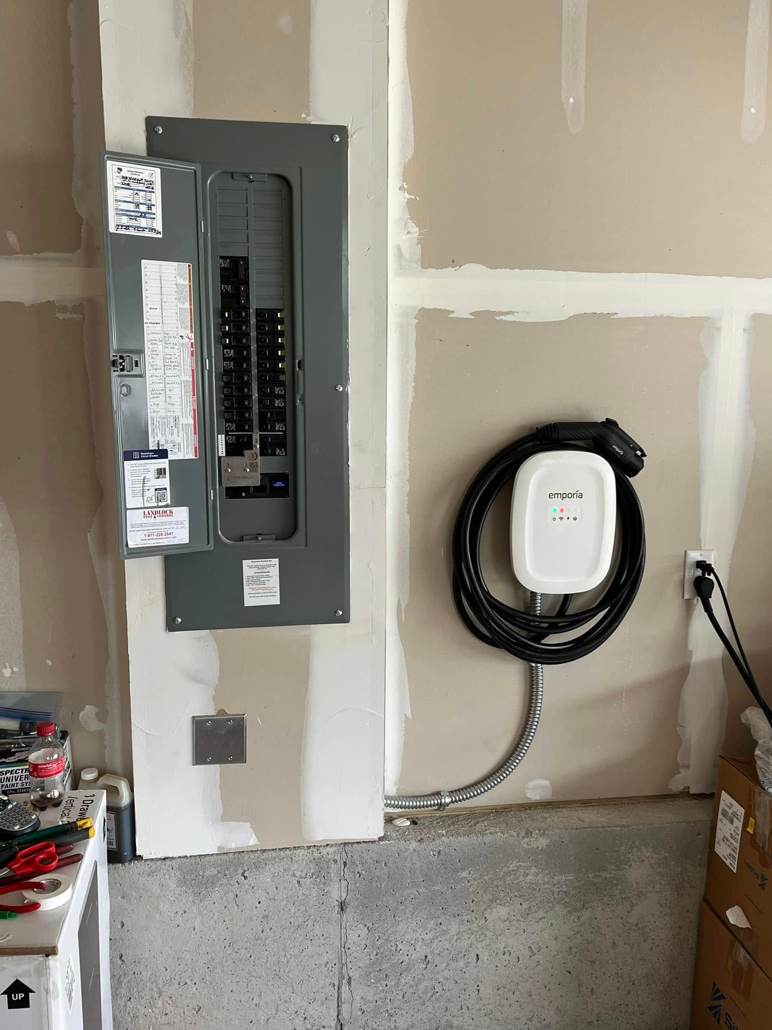 Electric panel and car charger mounted on a garage wall. The charger has a black coiled cable.