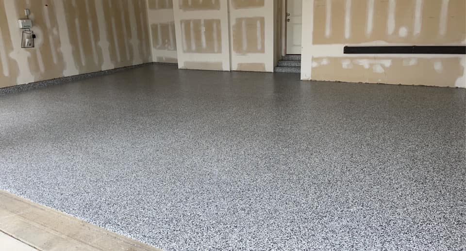 Gray speckled epoxy garage floor. Bare walls with unfinished drywall surround the floor.