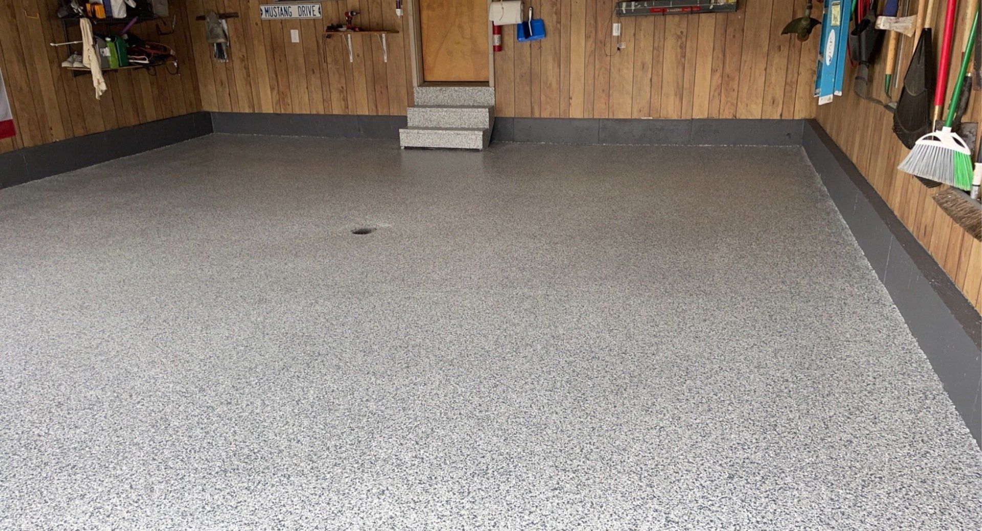 Gray speckled epoxy floor in an unfinished garage with exposed drywall walls.
