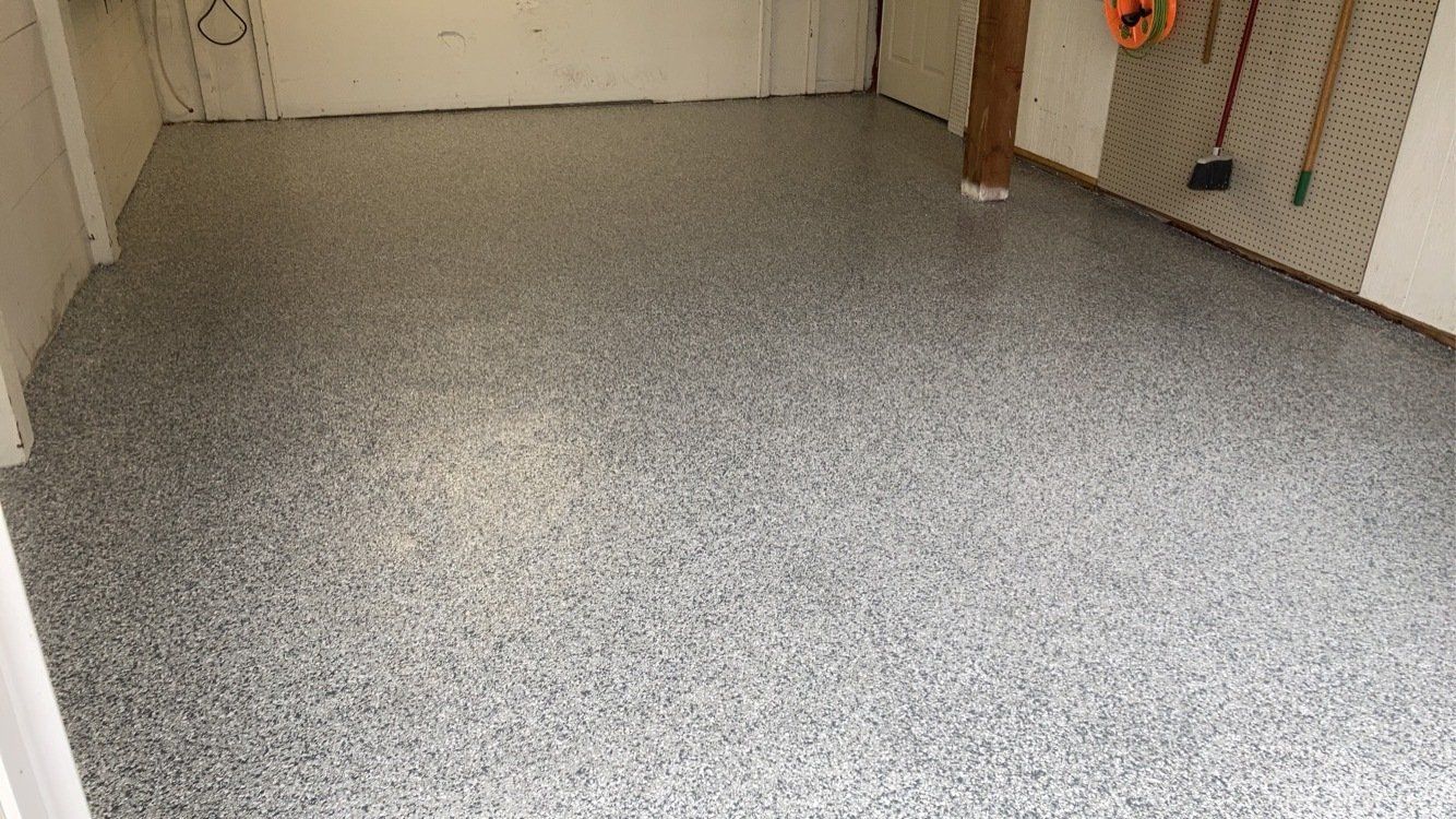 Gray speckled epoxy floor in a room. The room has white walls and some tools hanging on the wall.
