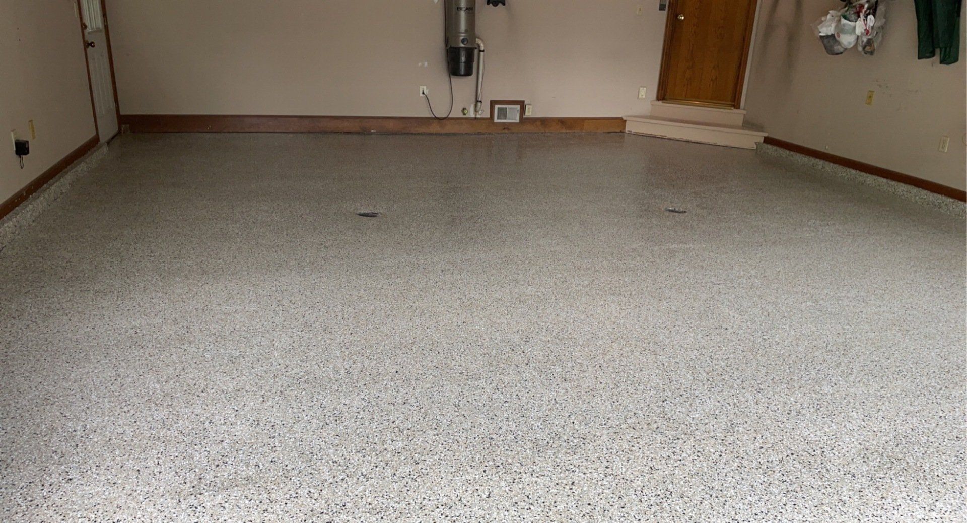 A garage with a speckled, light-colored epoxy floor, with a closed wooden door visible in the background.
