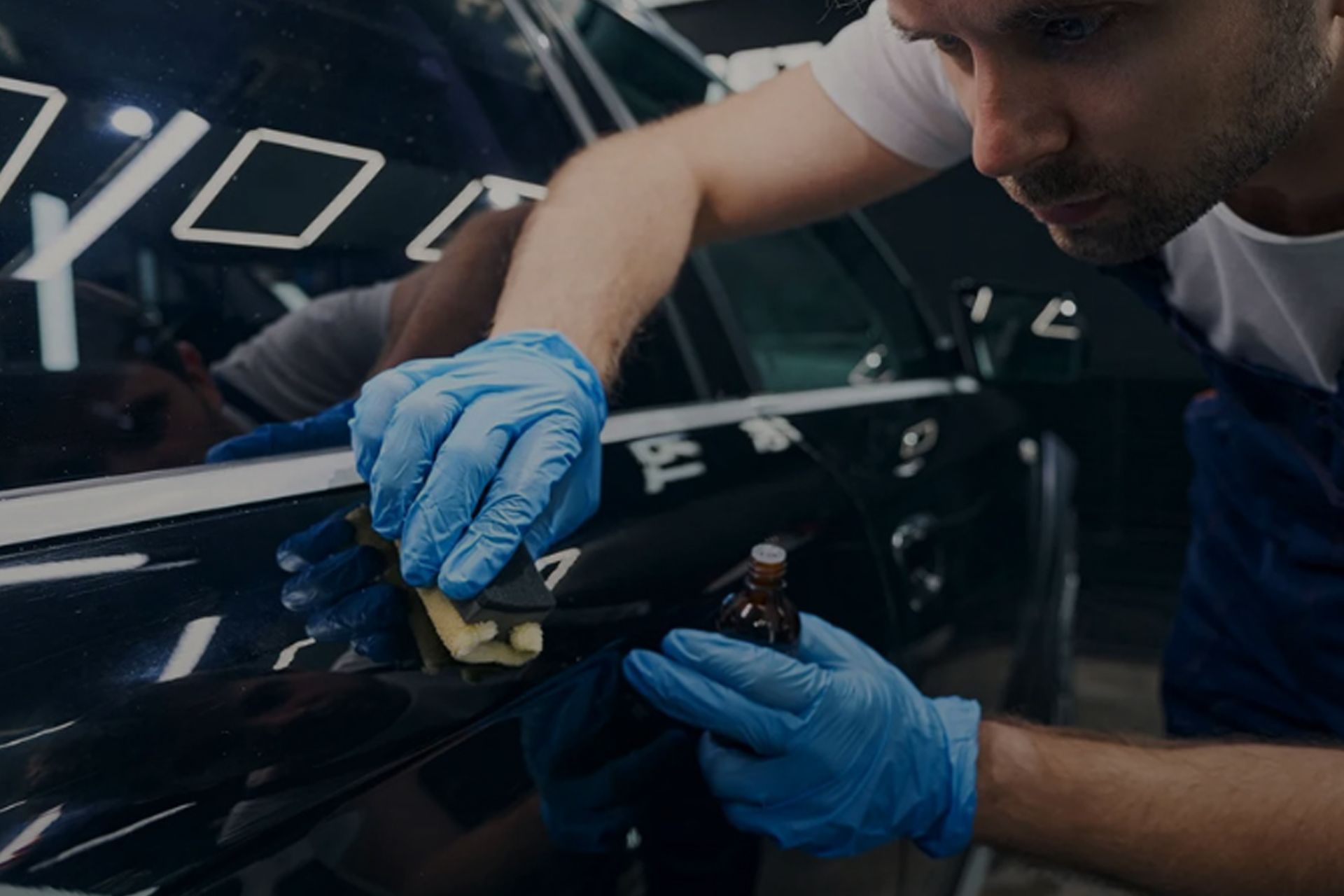 Person in blue gloves applies sealant to a black car.