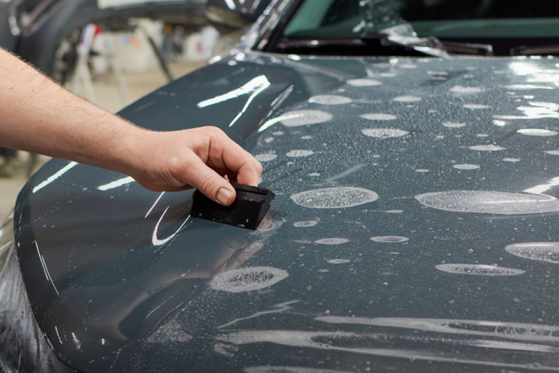 Hand applying protective film to a car hood, using a squeegee tool.