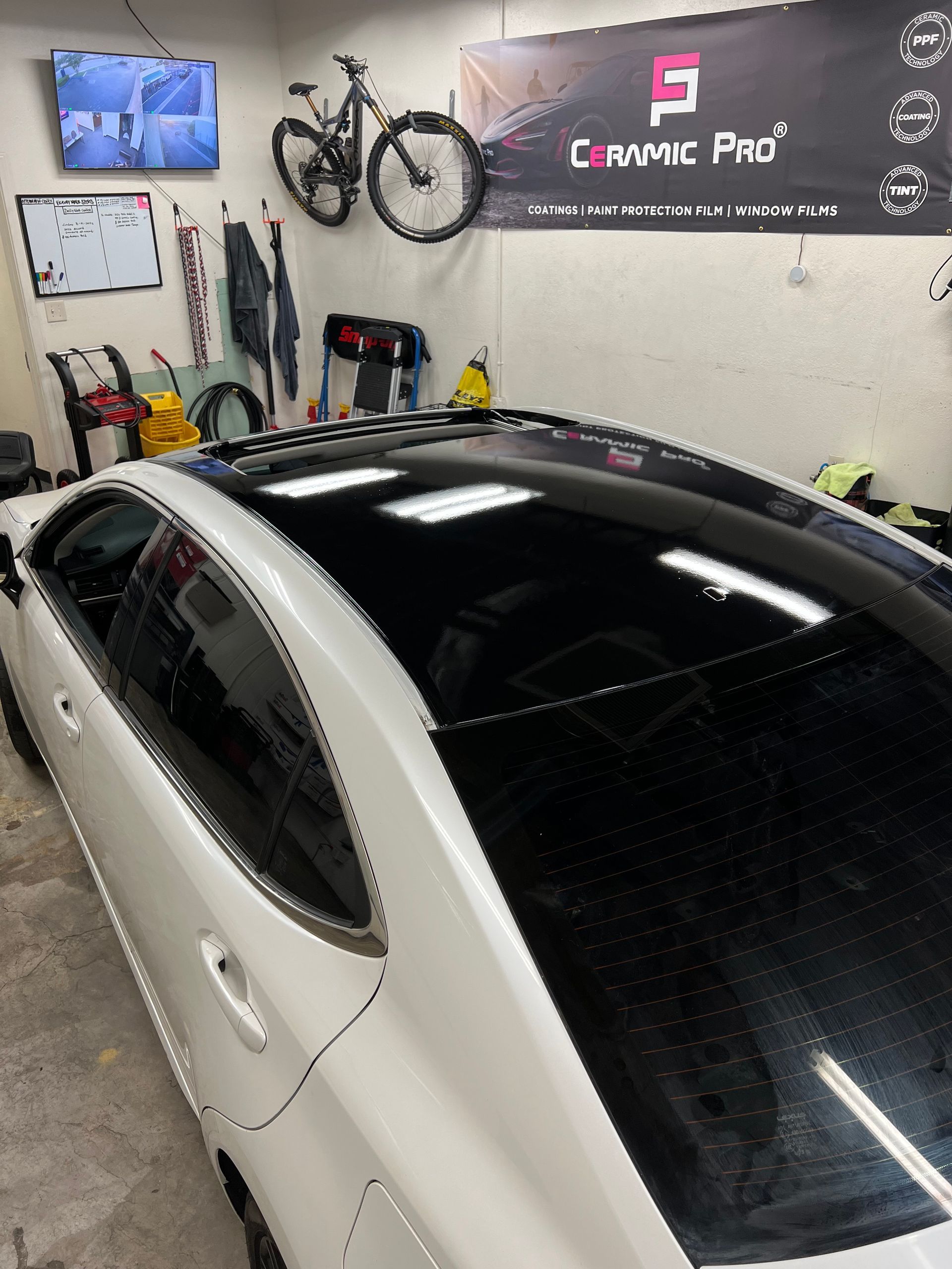 White car in a garage with wall-mounted bicycle, tools, and a black “Lynk Pro” banner above.