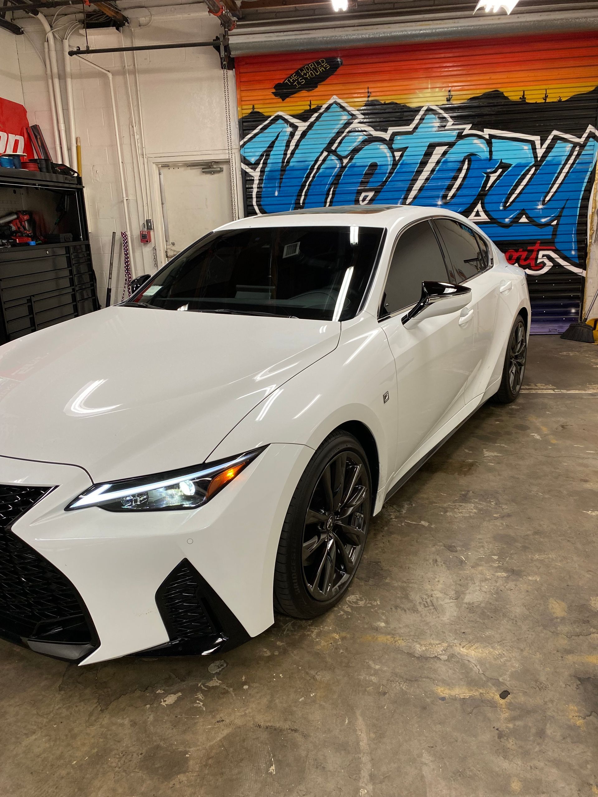 White luxury sedan in a garage with colorful wall graffiti and reflective black wheels