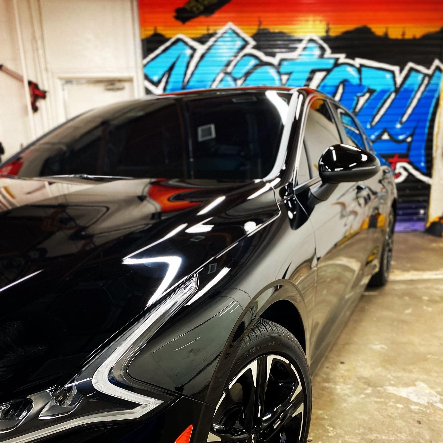 Black sports coupe in a garage with colorful graffiti wall behind it