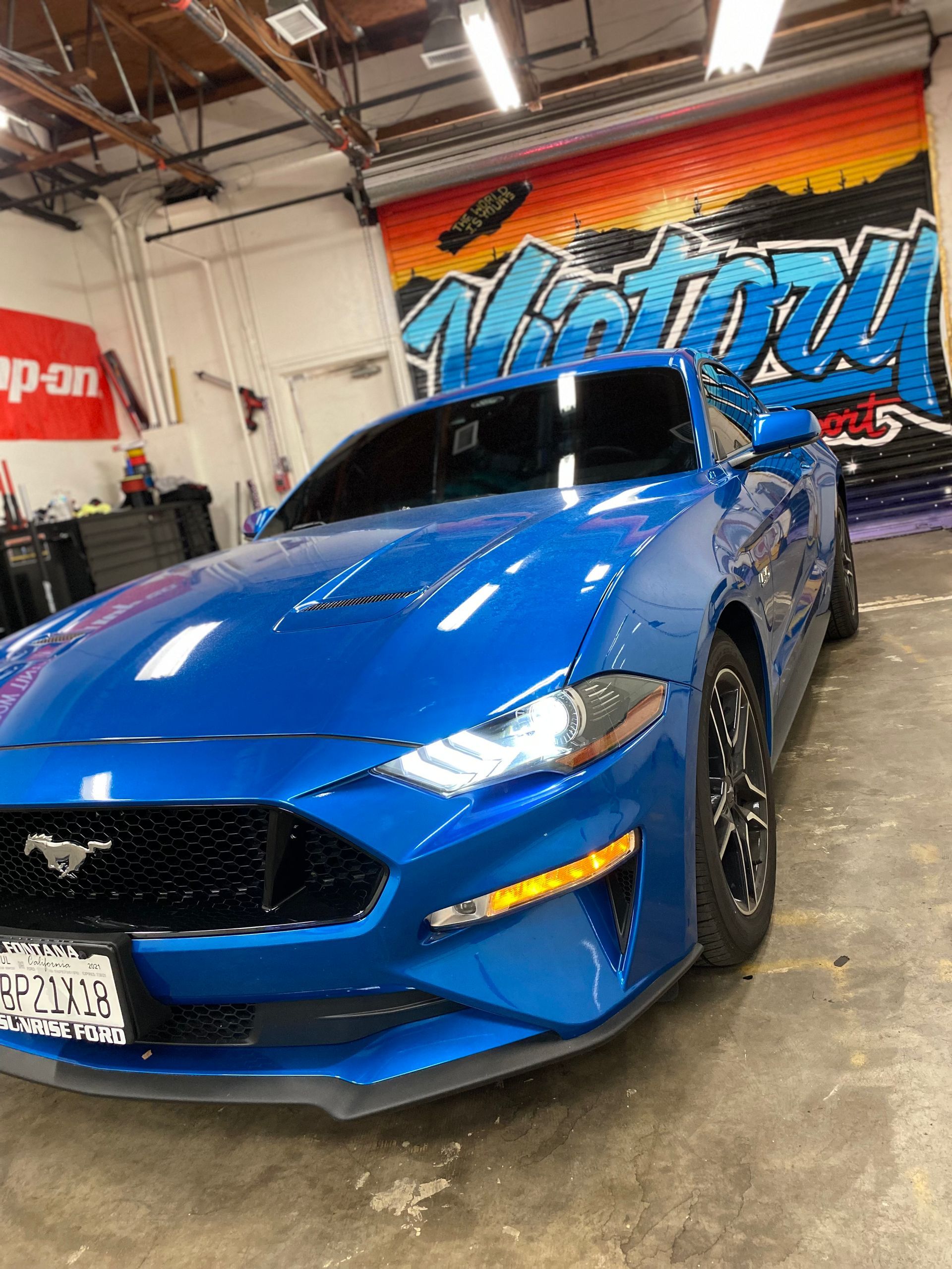 Blue sports car in a garage with a colorful graffiti wall behind it
